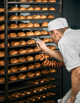 Bäcker von Bäckerei Schrott prüft frisch gebackene Brotlaibe auf einem hohen Backblechwagen.