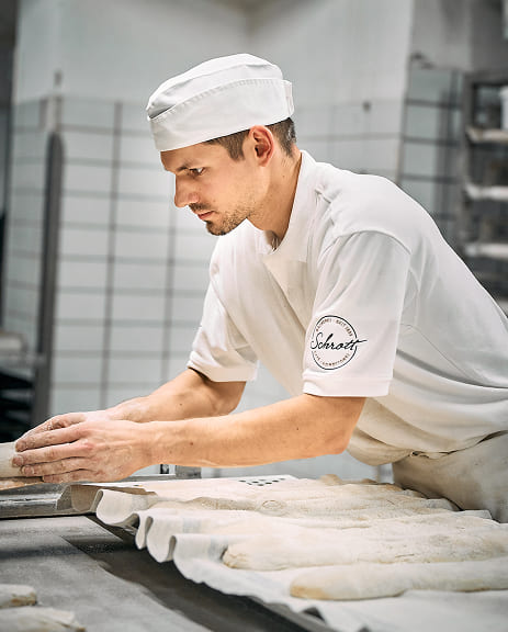 Bäcker von Bäckerei Schrott bearbeitet Teig in der Backstube mit konzentrierter Handarbeit.