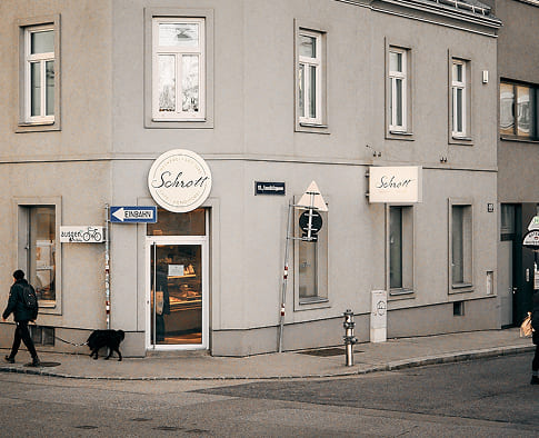 Außenansicht der Bäckerei Schrott mit Filiallogo über dem Eingang und Blick auf die Brot- und Gebäckauslage im Fenster.