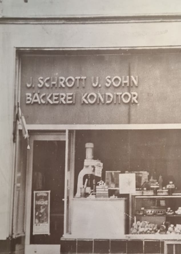 Historische Filiale von Bäckerei Schrott mit der Aufschrift „J. Schrott u. Sohn Bäckerei Konditor“ und Schaufenster mit Brot, Gebäck und Mehlspeisen.